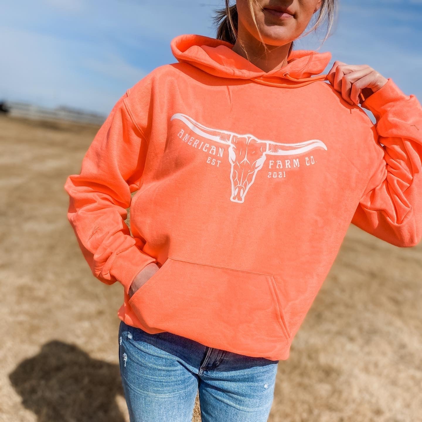 Woman displaying neon orange skull hoodie wearing jeans outside